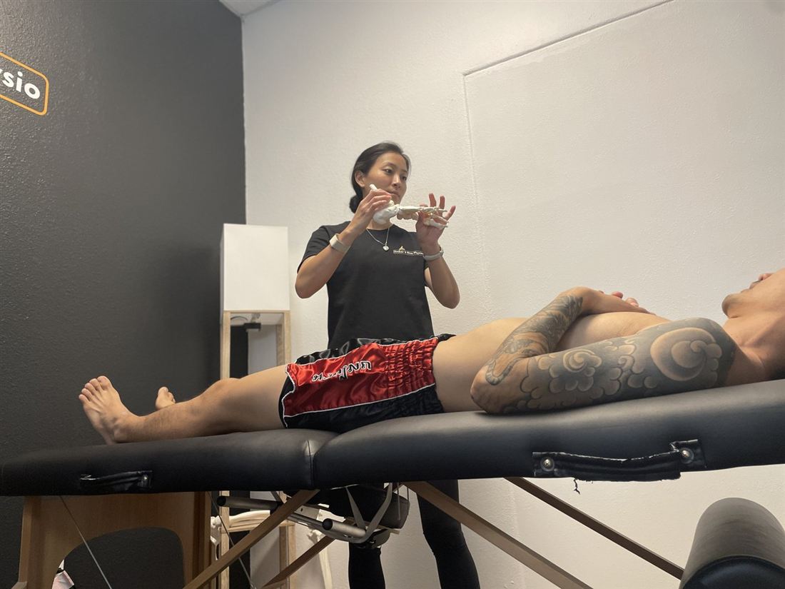 Dr. Ko holding a model of the foot and ankle while explaining it to a client on the treatment table