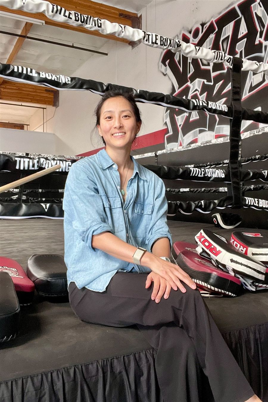 Dr. Lorrain Ko sitting on the edge of a boxing ring, smiling